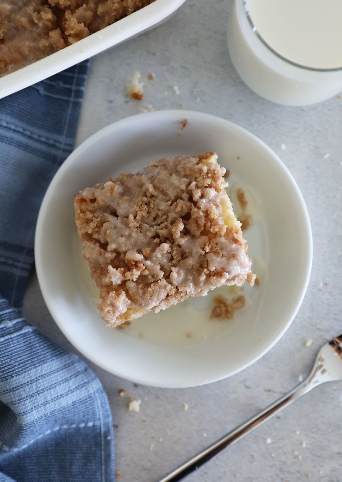 Bird's eye view of a slice of coffee cake on a white plate next to a blue towel and a fork. 