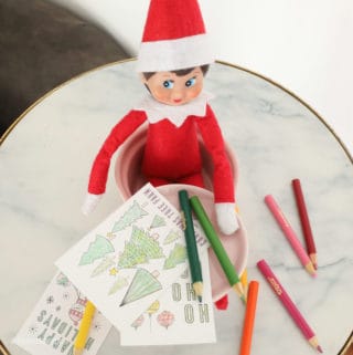 Elf on a shelf coloring some small christmas coloring sheets with mini colored pencils.