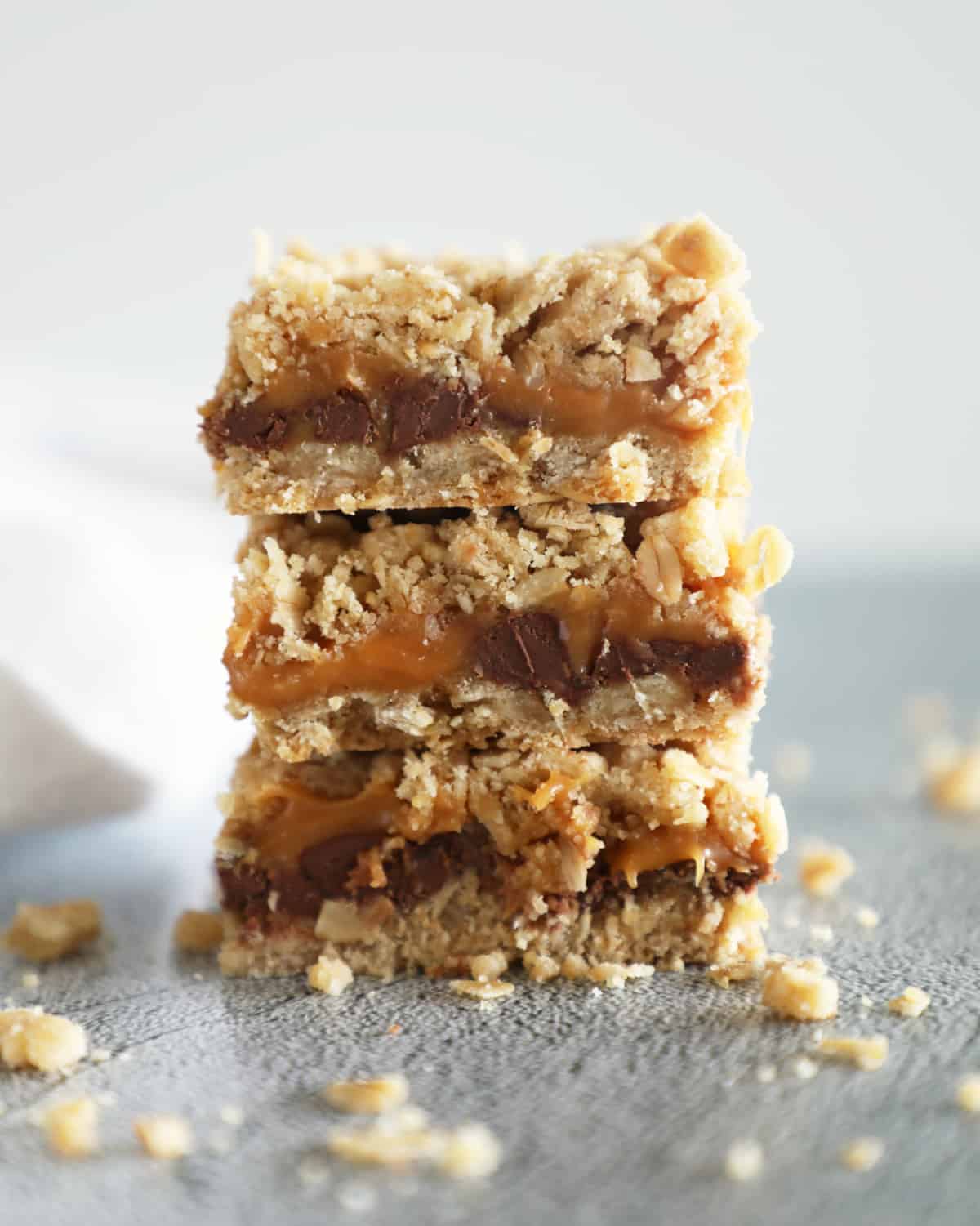 Carmelitas, layered oatmeal chocolate and caramel dessert bars, stacked on top of each other with crumbs surrounding. 