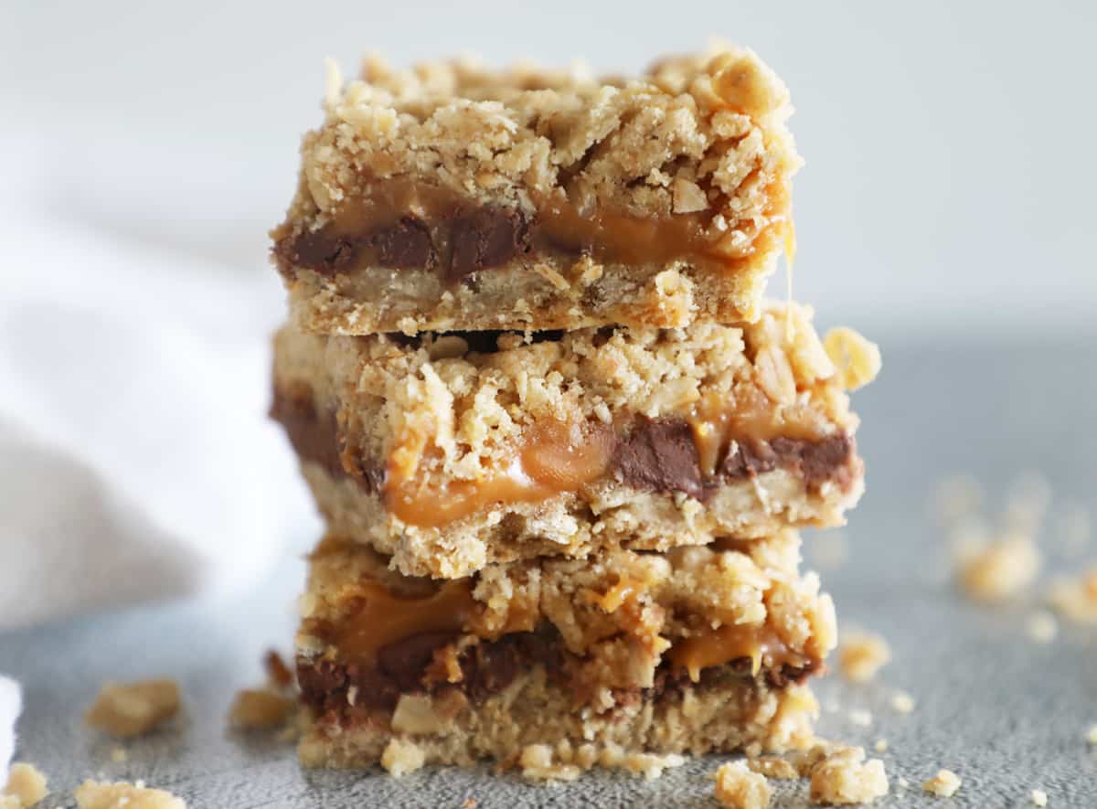 Three Carmelita bars stacked on top of each other with crumbs on the countertop around them
