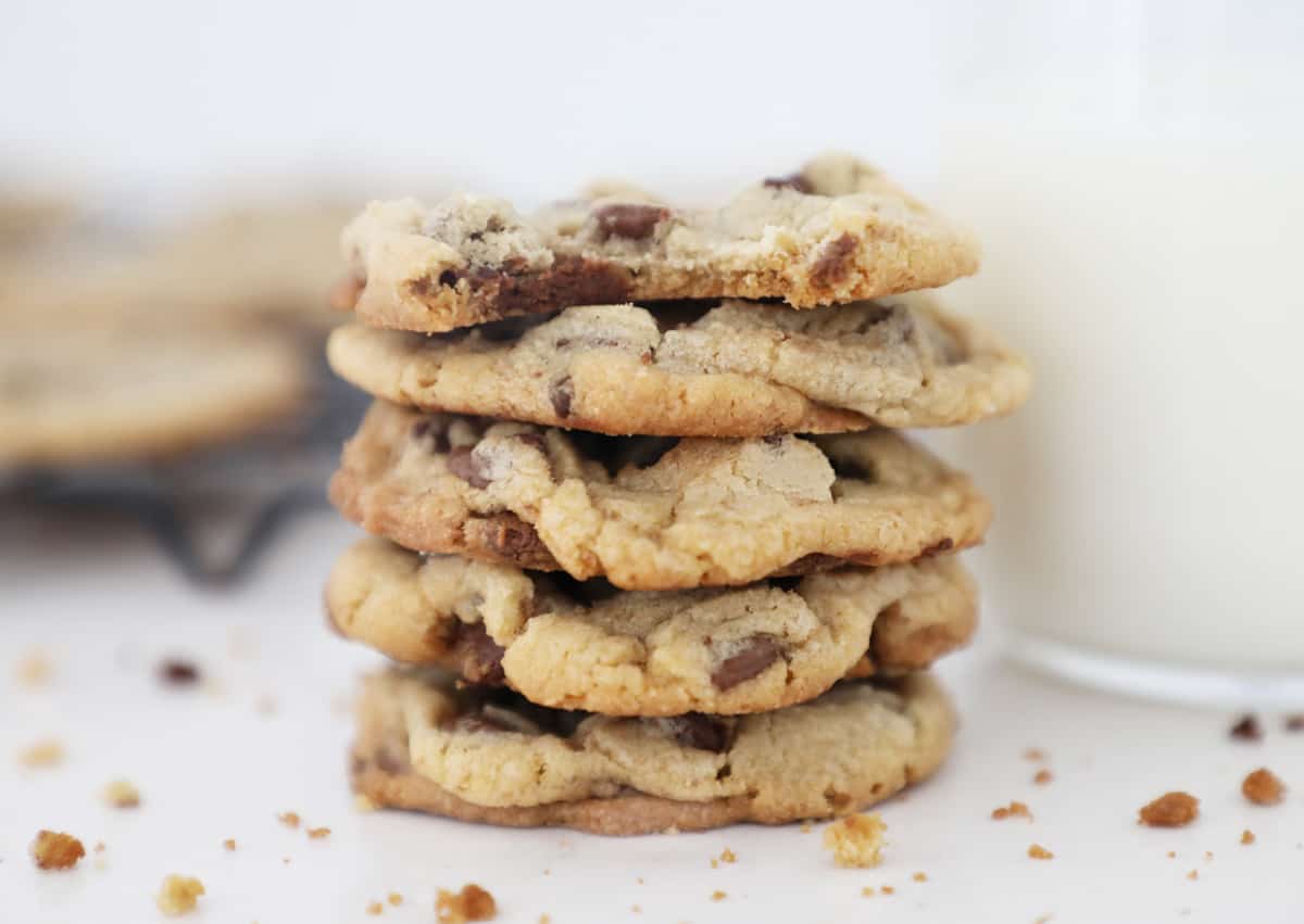 A small stack of chewy chocolate chip cookies next to a glass of milk. 