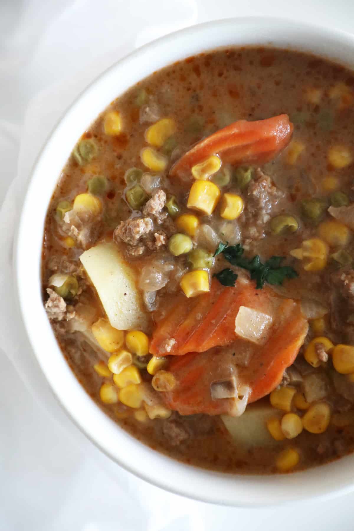 A close up view of a bowl of beef stew with carrots, peas, corn, onions and beef. 