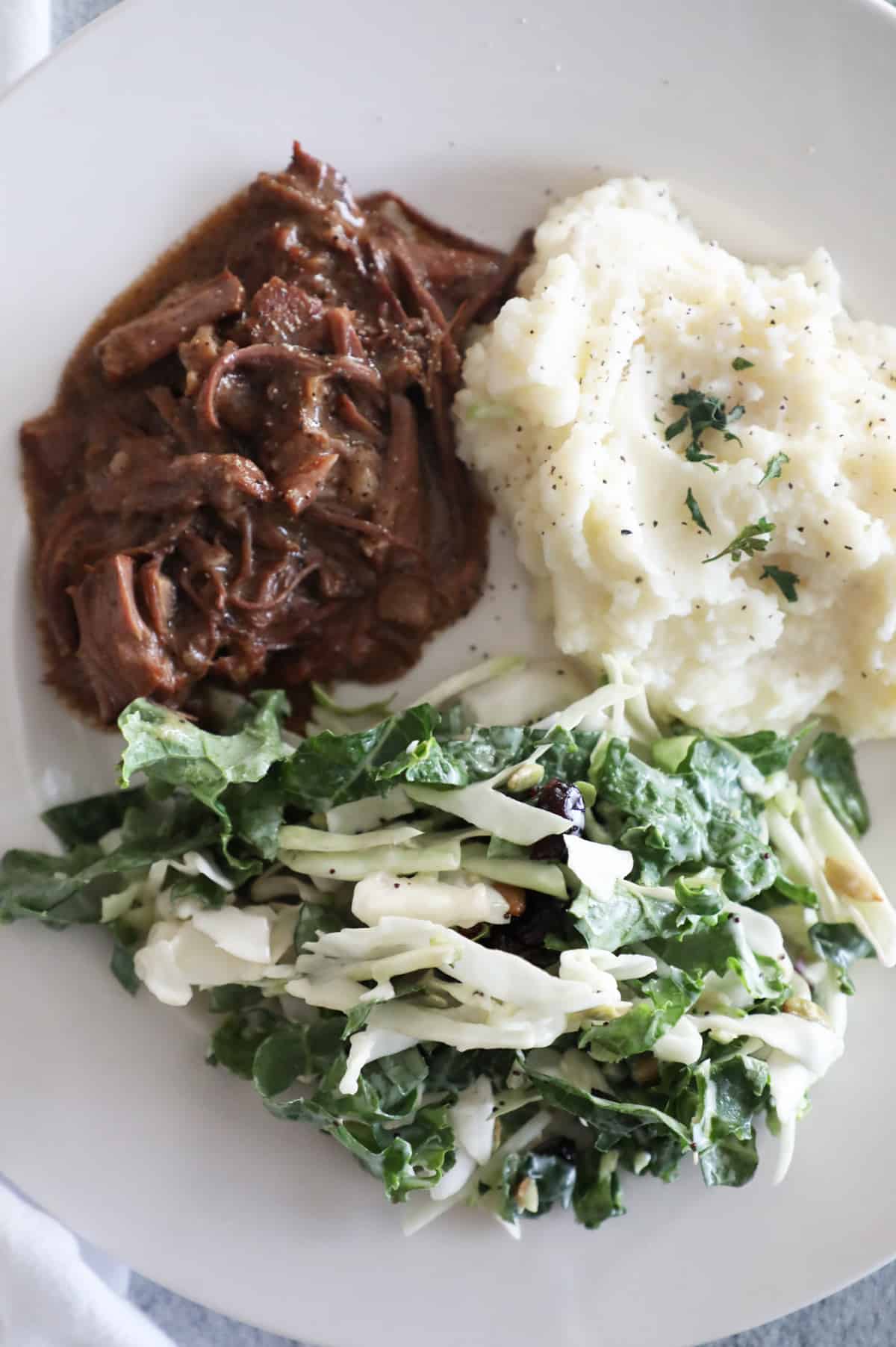 Close-up photo of pot roast, mashed potatoes and salad on a white plate. 