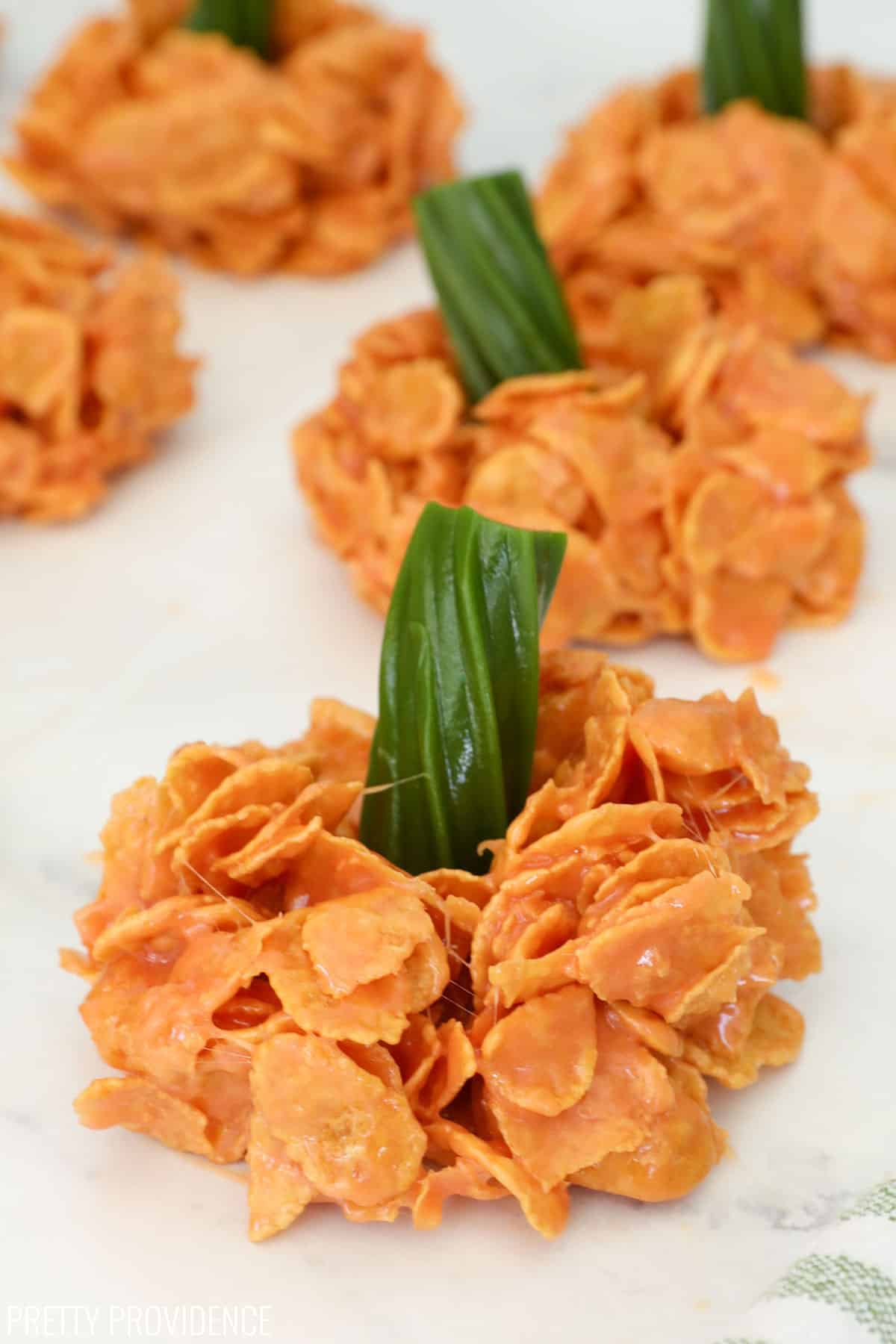 a close-up shot of a pumpkin-shaped treat made with cornflakes and melted marshmallow topped with a green licorice stem.