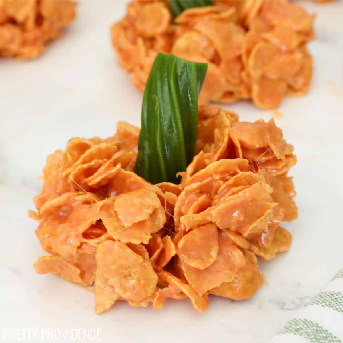 a close-up shot of a pumpkin-shaped treat made with cornflakes and melted marshmallow topped with a green licorice stem.