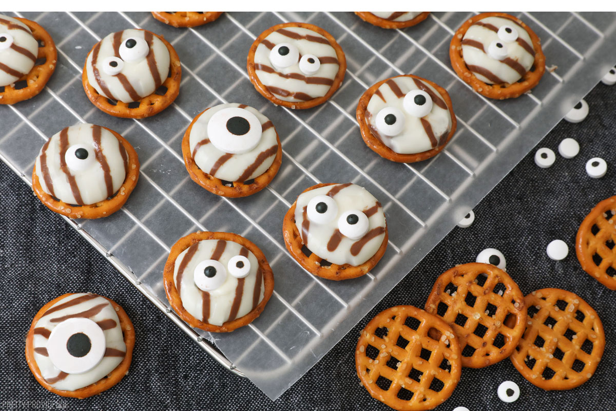 white chocolate striped hersheys hugs melted on to pretzels and topped with candy eyeballs resting on wax paper over a black runner.