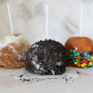 Three gourmet homemade caramel apples of differing varieties sitting on a kitchen counter.