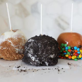 Three gourmet homemade caramel apples of differing varieties sitting on a kitchen counter.