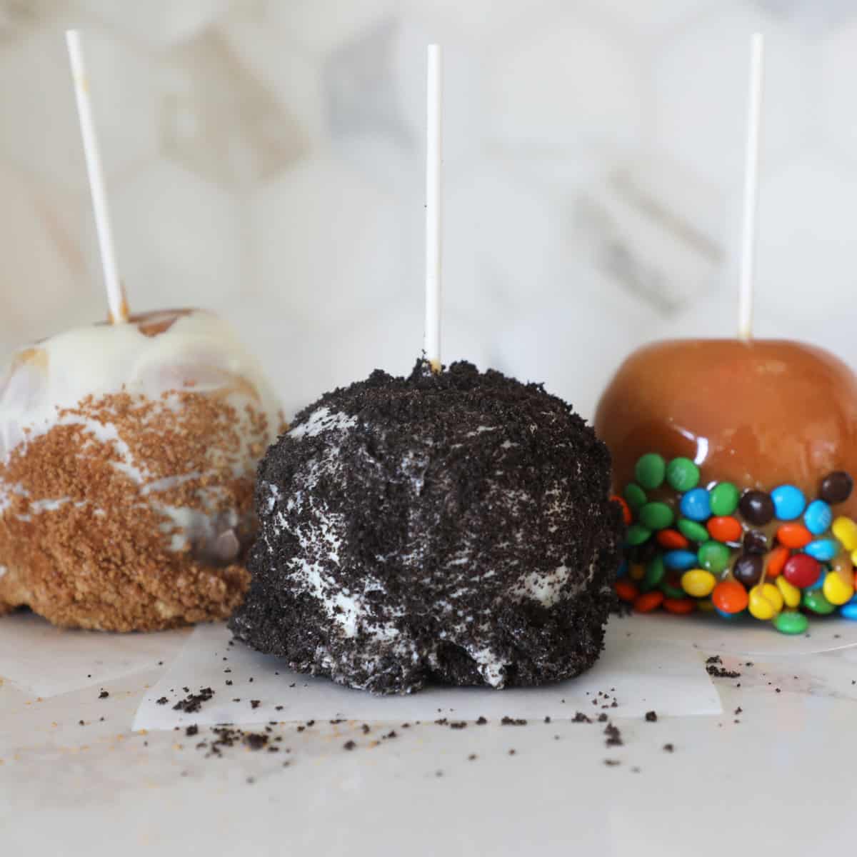 Three gourmet homemade caramel apples of differing varieties sitting on a kitchen counter. 