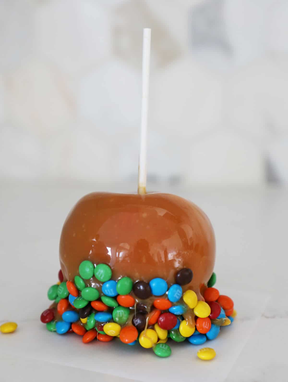 A close up photo of a homemade m&m covered caramel apple. 