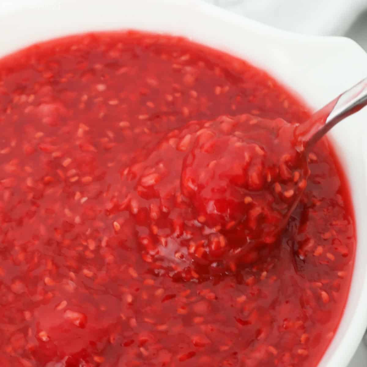 Raspberry pie filling in a white bowl, a big spoonful coming out of the bowl.