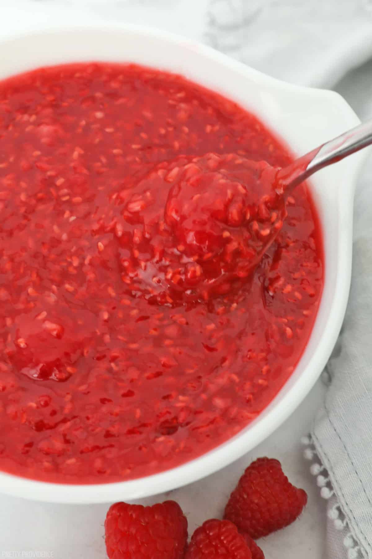 Raspberry pie filling in a white bowl, a big spoonful coming out of the bowl. 