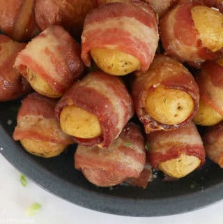 Bacon wrapped potatoes crispy and golden brown on a dark gray plate.