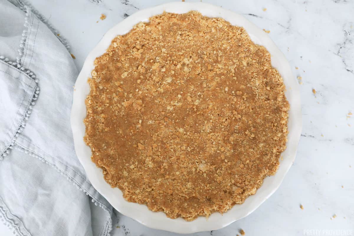 Graham cracker pie crust in a round pie dish with a scalloped edge.