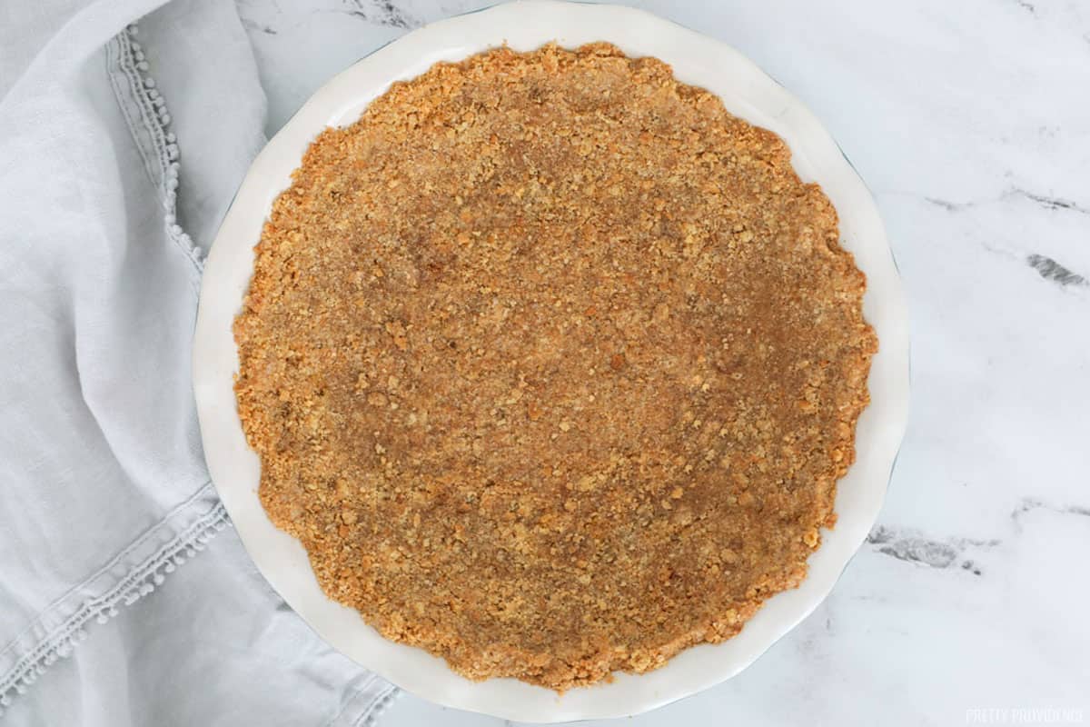 Graham cracker pie crust in a round pie dish with a scalloped edge.