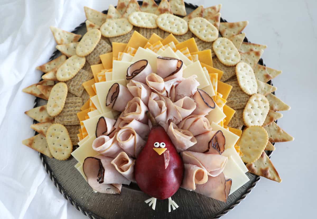 A cheeseboard styled like a turkey for thanksgiving on a white countertop.