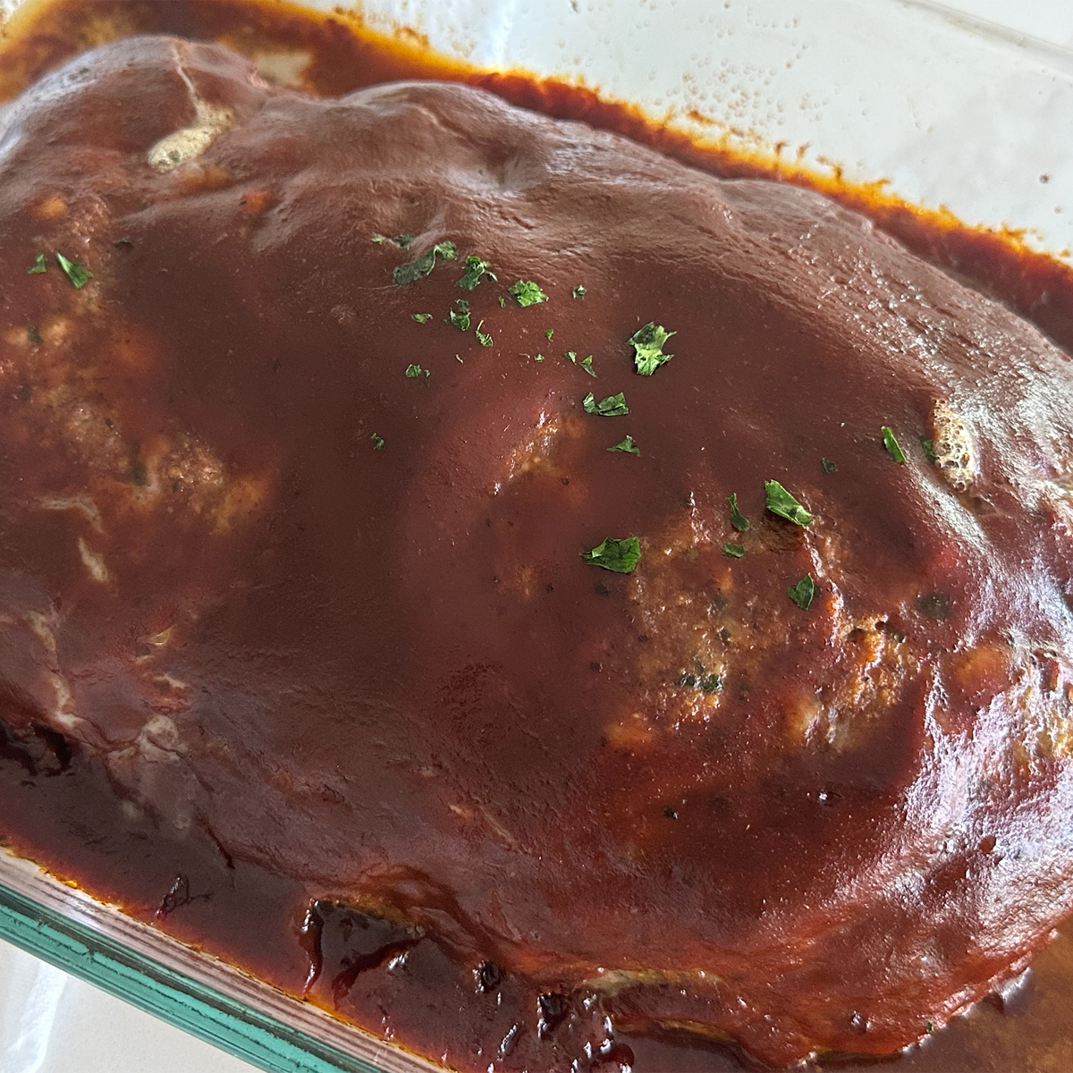 A sideview of homemade meatloaf in a glass 9x13 baking dish with parsley on top.