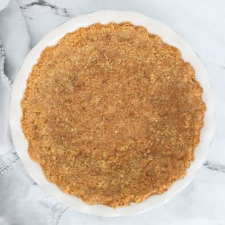 Graham cracker pie crust in a round pie dish with a scalloped edge.