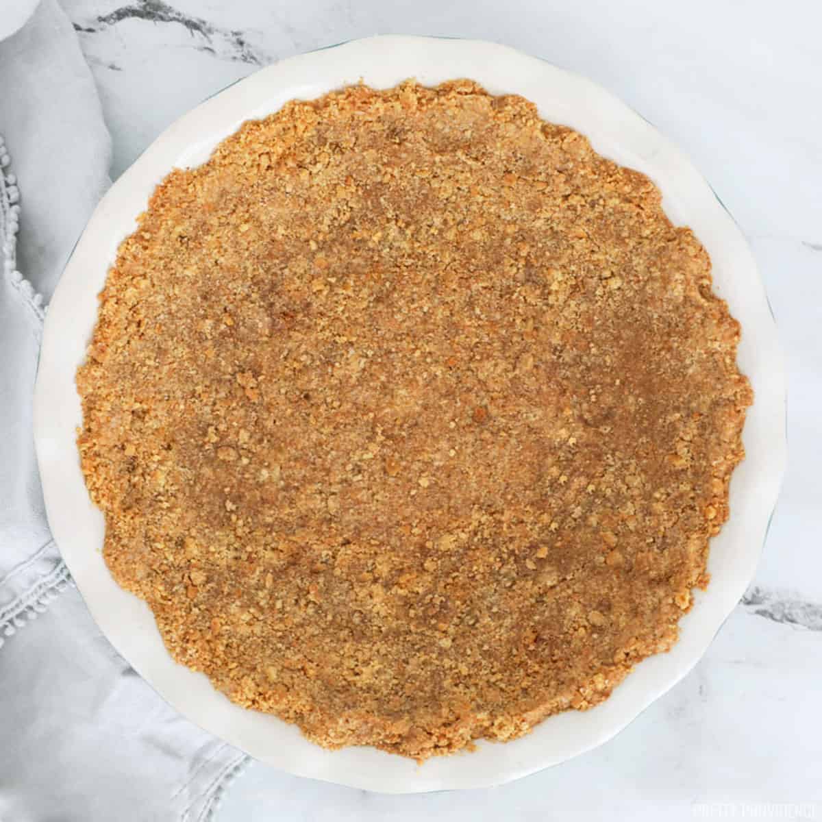 Graham cracker pie crust in a round pie dish with a scalloped edge. 