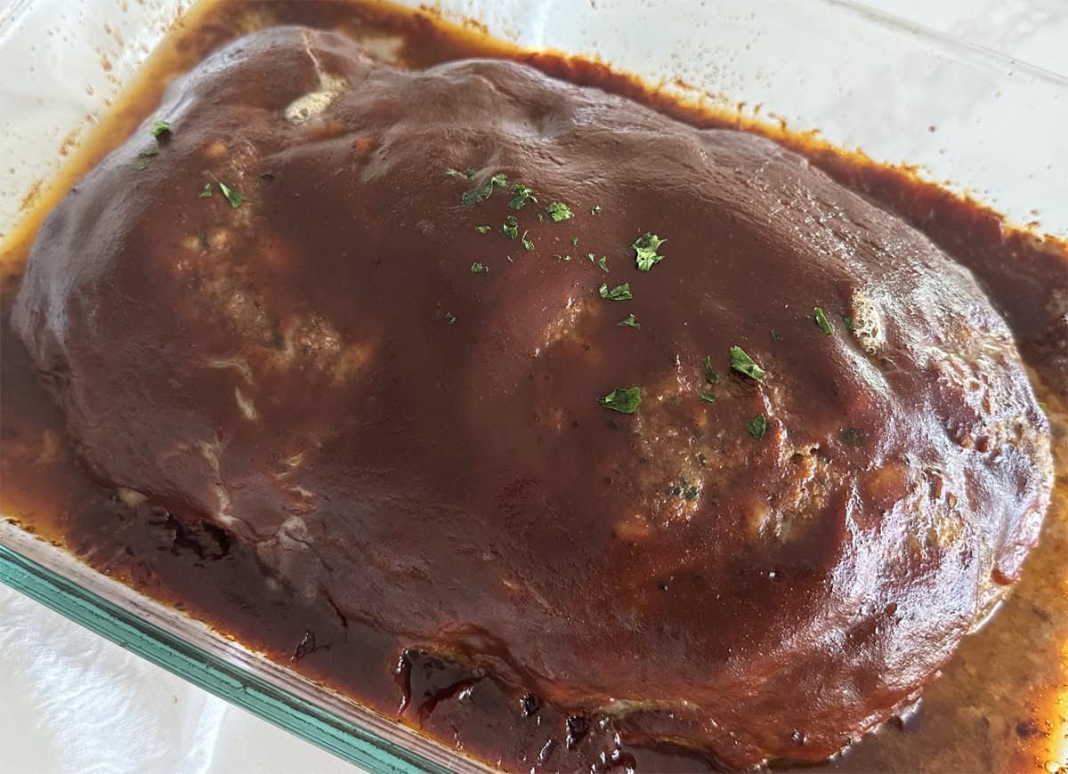 A sideview of homemade meatloaf in a glass 9x13 baking dish with parsley on top. 