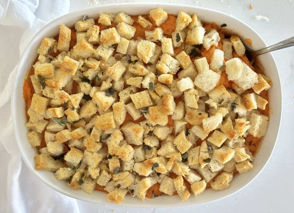 A savory sweet potato casserole topped with homemade bread cubes and a spoon stuck in the side. 