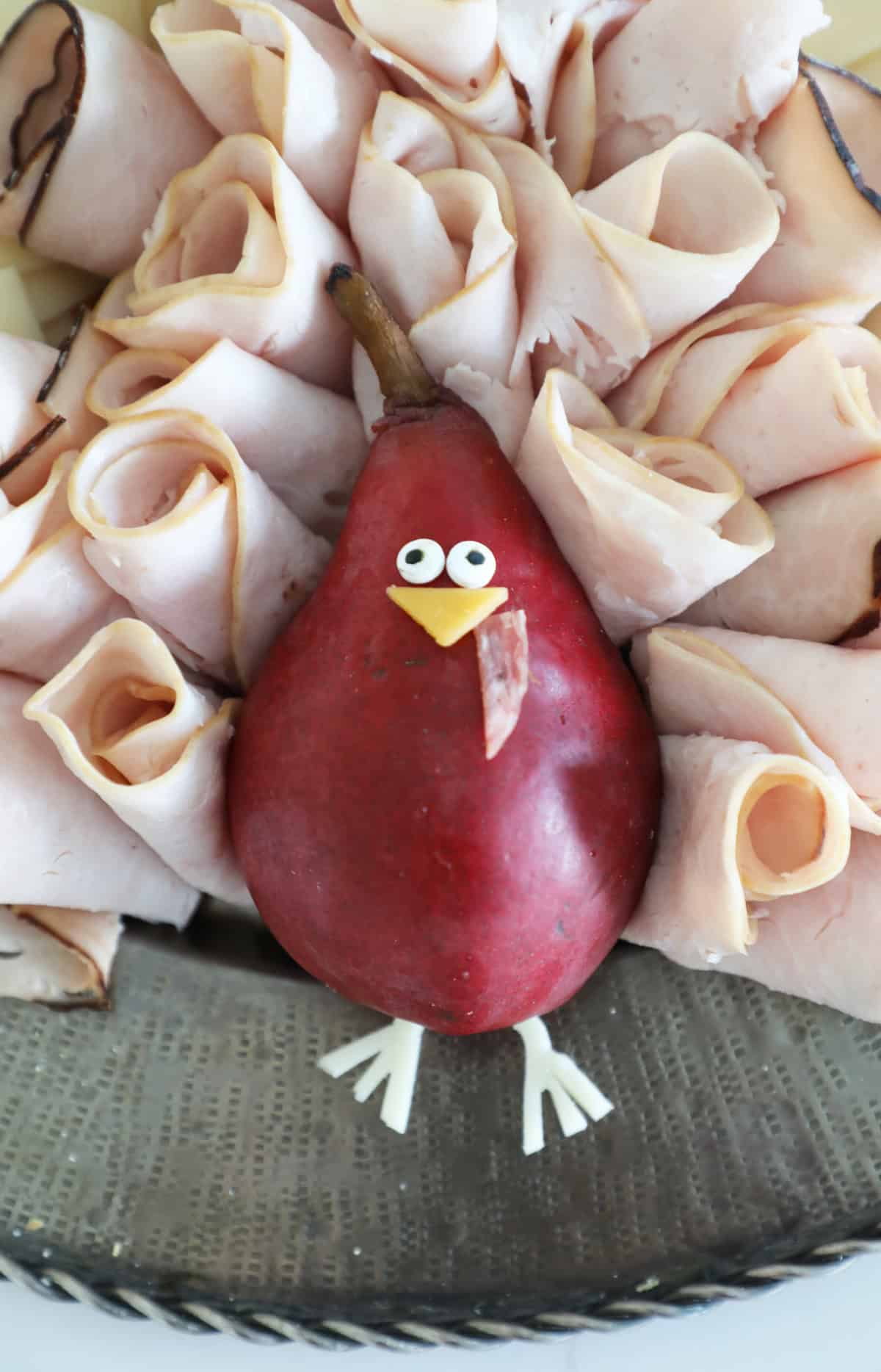 A turkey made from a pear surrounded by lunchmeat on a Thanksgiving cheese board. 