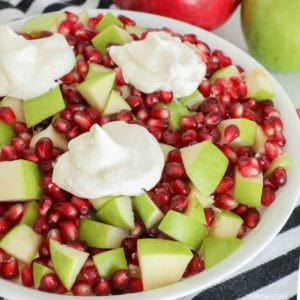 Fruit salad made with granny smith apple cubes and pomegranate seeds mixed with cool whip with dollops of cool whip on top.