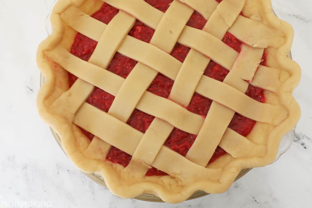 Homemade raspberry pie with filling and unbaked pie crust with criss-cross pattern ready to go in the oven.