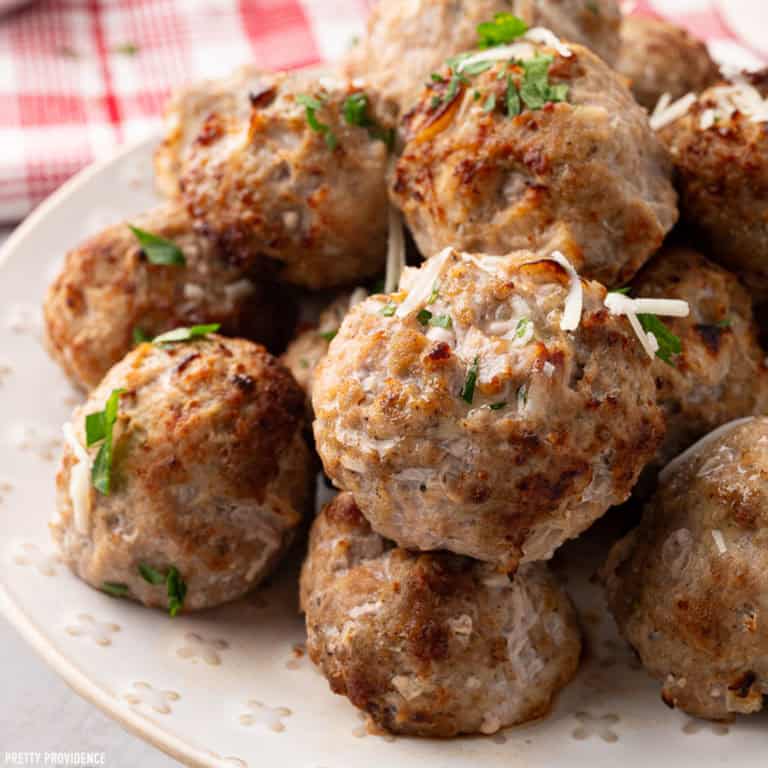Turkey meatballs on a cream-colored plate garnished with parsley and parmesan cheese.