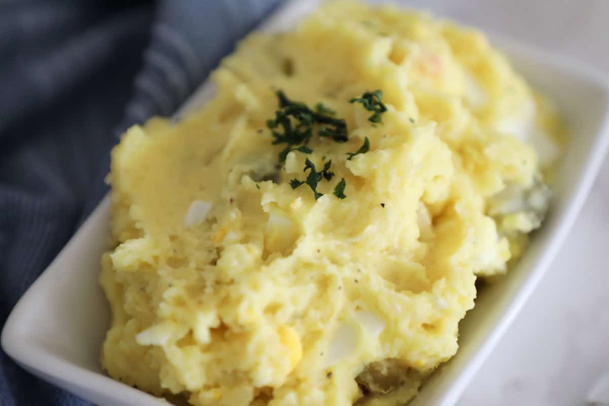 A small dish of potato salad with eggs and green olives. 