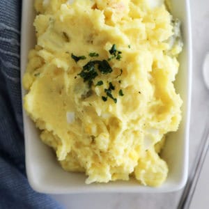 A photo of potato salad in a small white dish next to a blue towel.