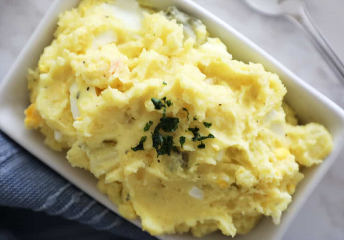 A small white dish of potato salad on a marble countertop. 