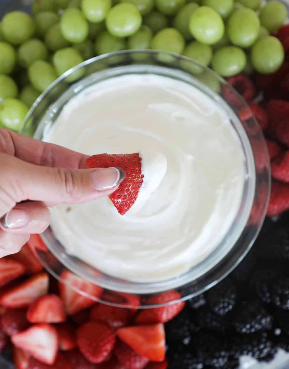 A hand holding a dipped strawberry over a bowl of cream cheese fruit dip. 