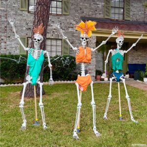 Three skeletons in a Halloween display wearing swimsuits and headpieces posed like they are waving to a crowd.