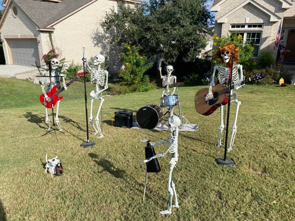 Skeletons dressed up like a rock band with instruments in a front yard.
