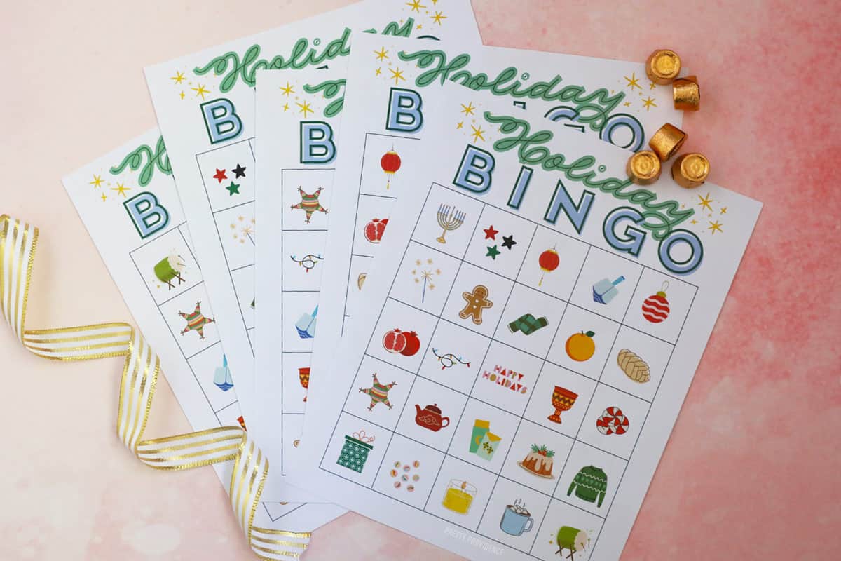 Holiday bingo cards representing winter holidays on a pink background with gold-wrapped candy beside it.