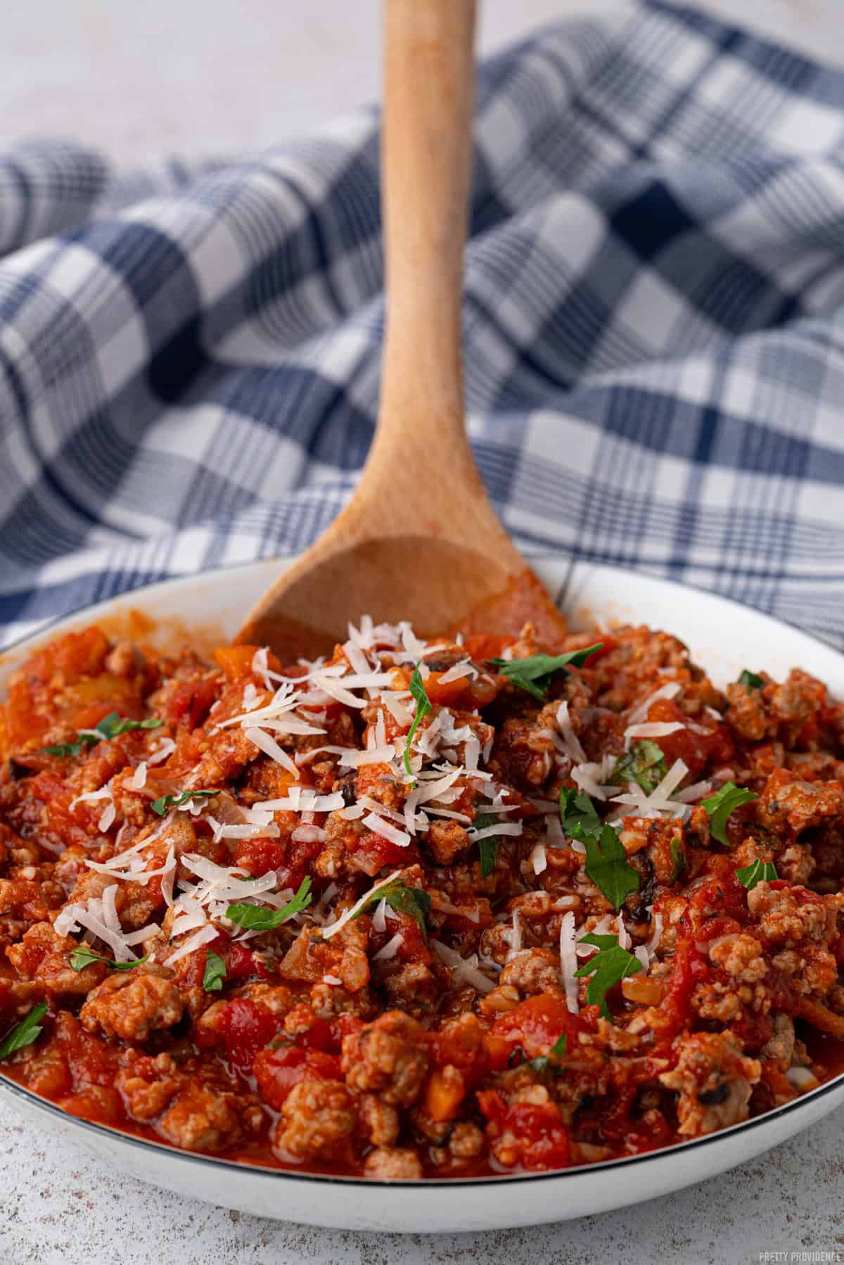 Turkey bolognese sauce close up shot of sauce with fresh basil and grated parmesan on top, being lifted up with a wooden spoon.