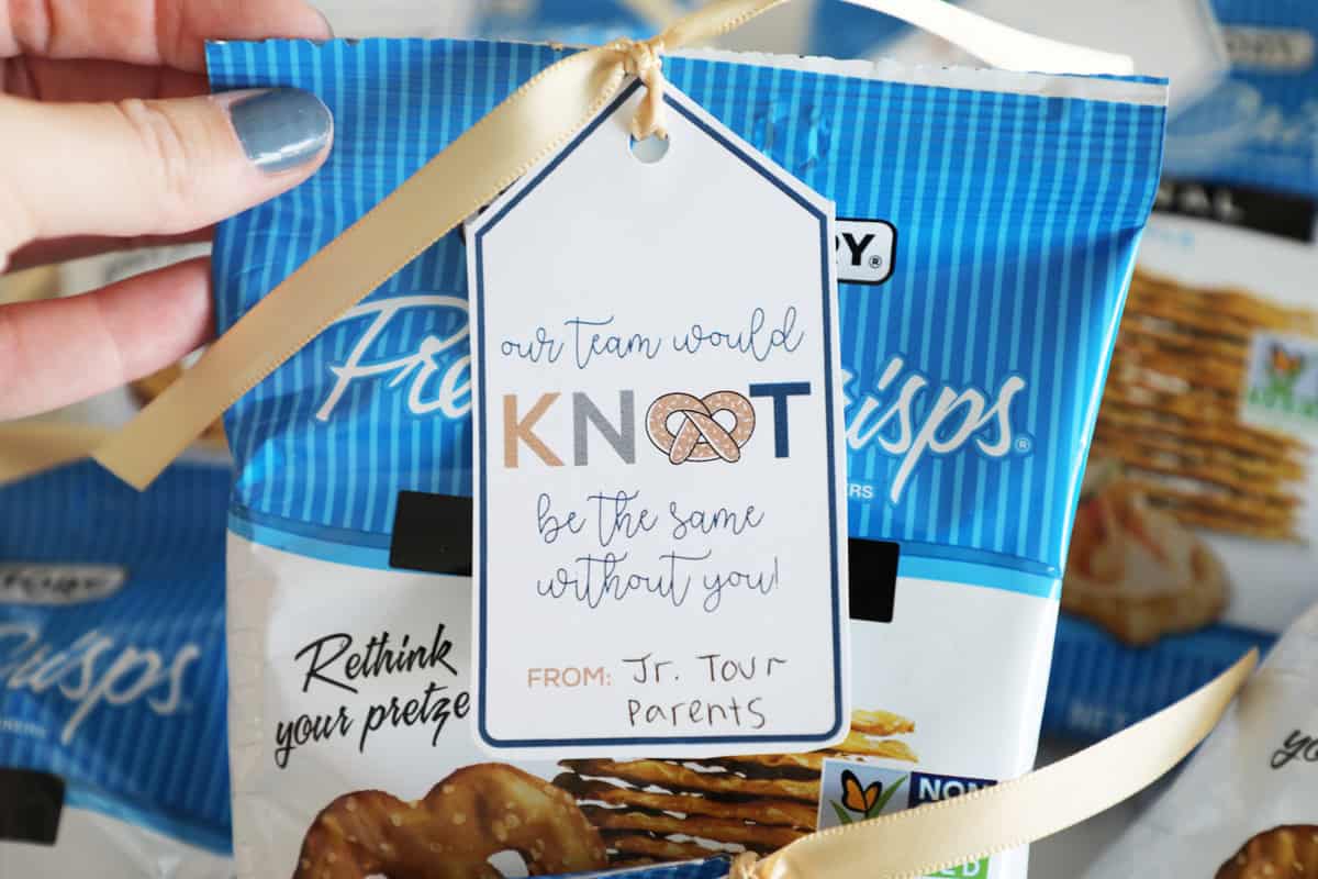 A blue painted thumb holding up a bag of pretzels with a cute tag.